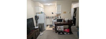A kitchen area with a refrigerator, microwave, and a table with a computer on it.