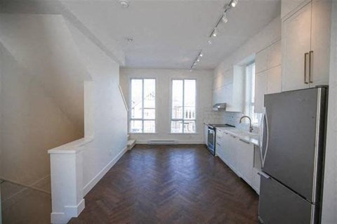 A kitchen with a refrigerator, sink, and wooden floors.