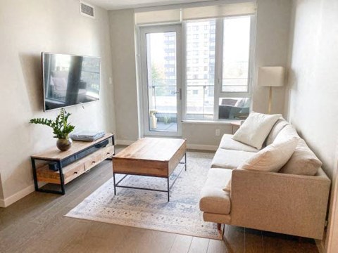A living room with a couch, coffee table, and a flat screen TV mounted on the wall.