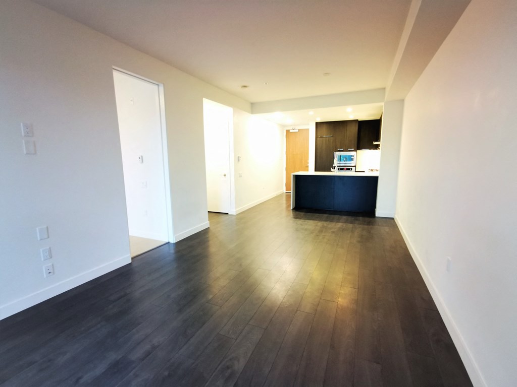 an empty living room with wood floors and a kitchen