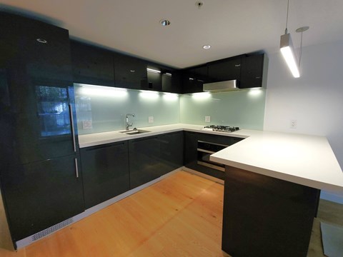 A modern kitchen with black cabinets and a wooden floor.