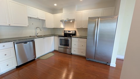 A kitchen with white cabinets and a wooden floor.