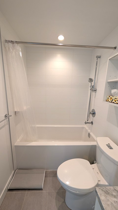 A white toilet sits in a bathroom next to a bathtub.