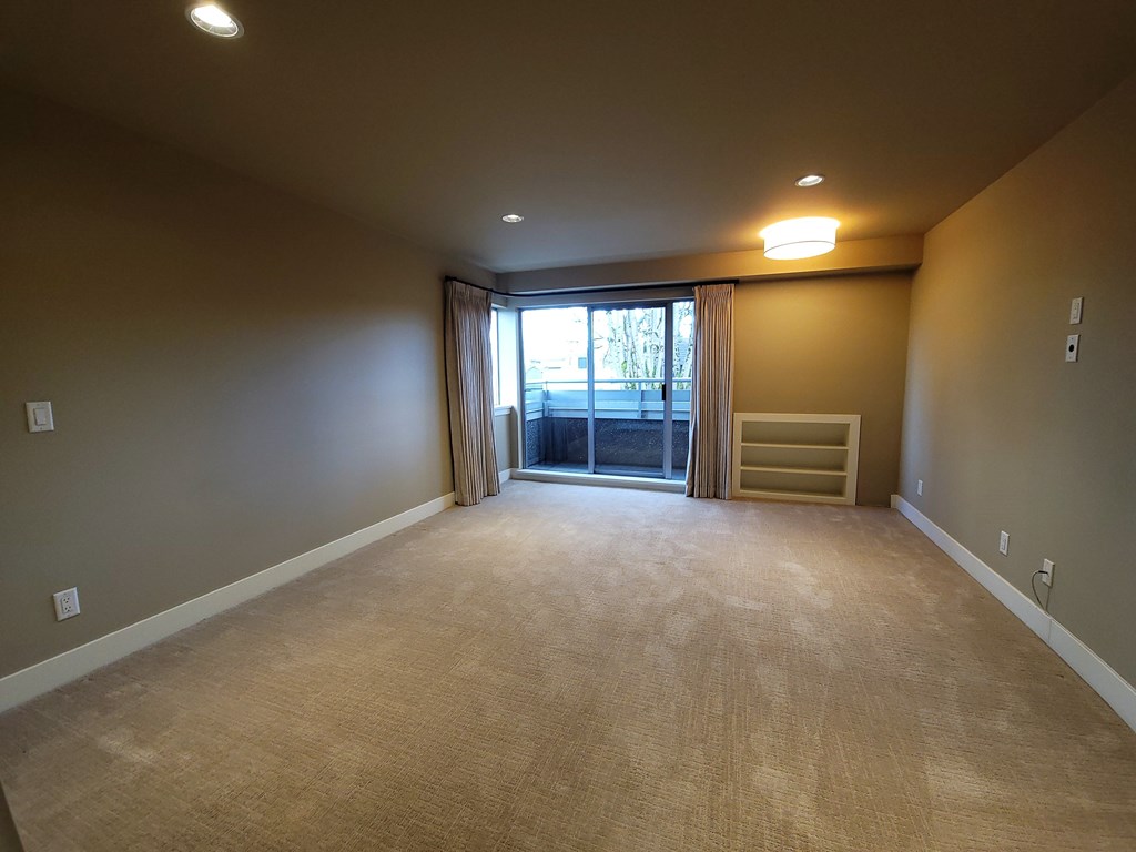 A room with beige carpet and a window with curtains.