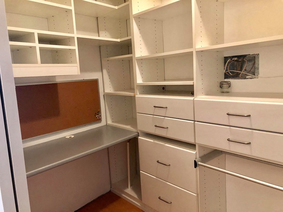 a walk in closet with white shelves and drawers