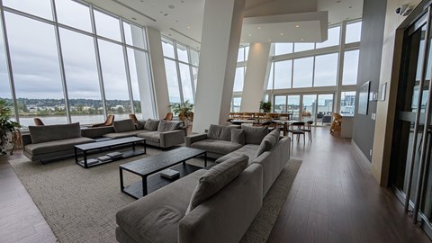 A spacious living room with grey couches and a glass table.