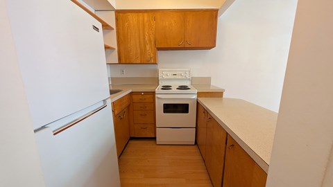 A white refrigerator is on the left side of a kitchen with wooden cabinets and a white stove top oven.