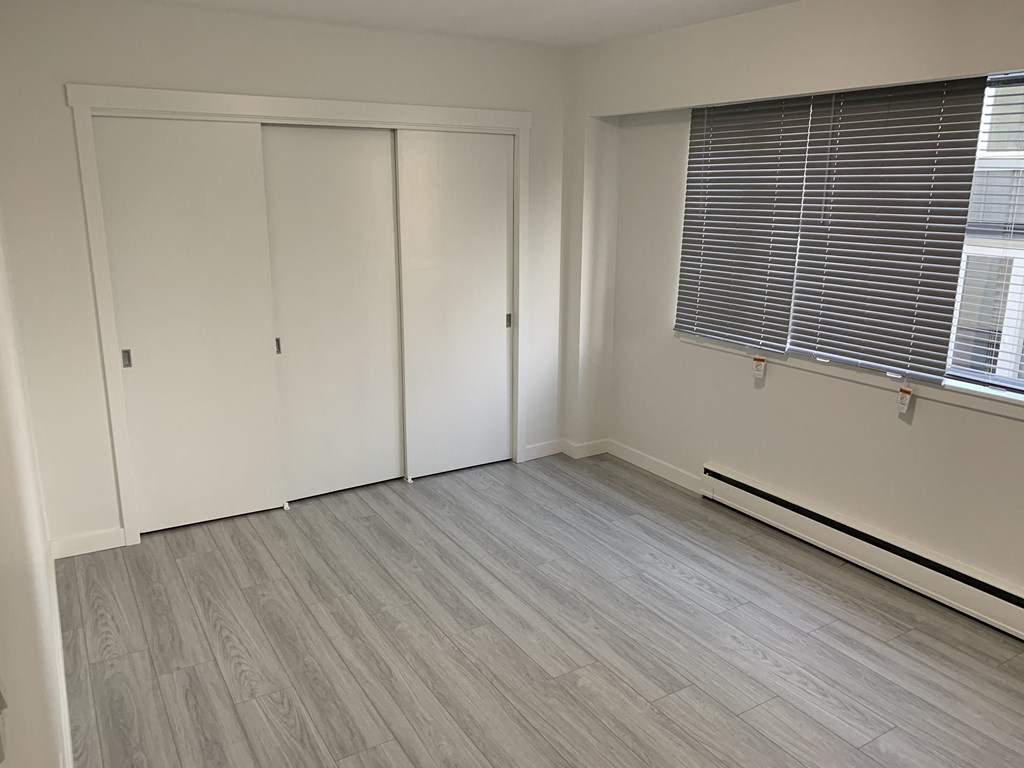 a bedroom with white walls and wood floors and a window