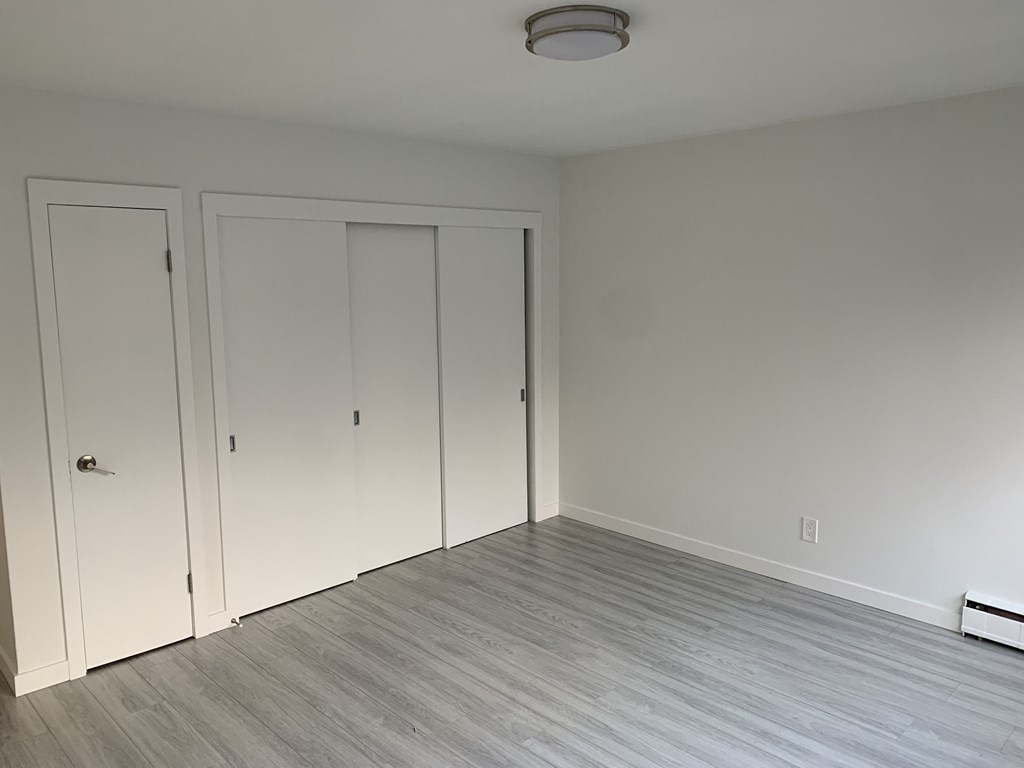 a bedroom with white walls and wood flooring and two closet doors