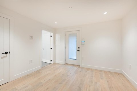 A room with white walls and wooden flooring with three doors.