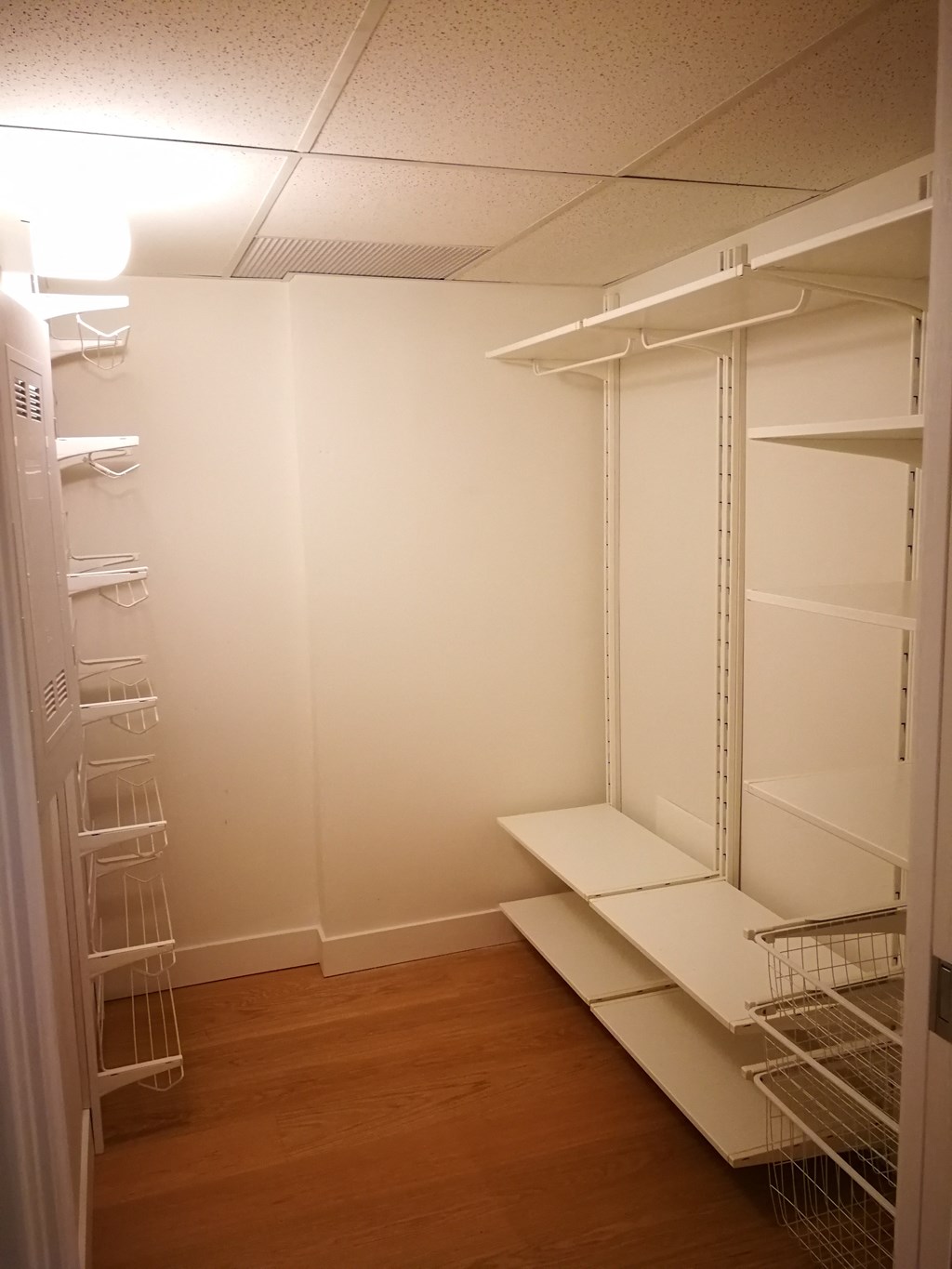 a walk in closet with white shelves and a wood floor
