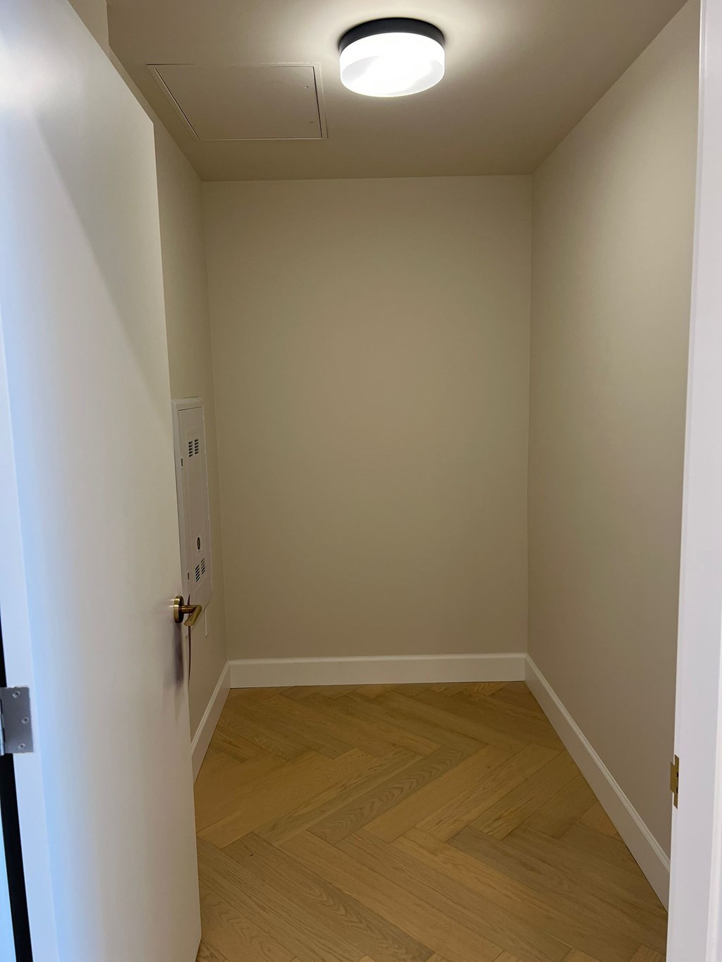 A white door with a gold handle is on the left side of a hallway with wooden floors and white walls.