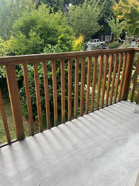 A wooden railing on a concrete floor with trees in the background.