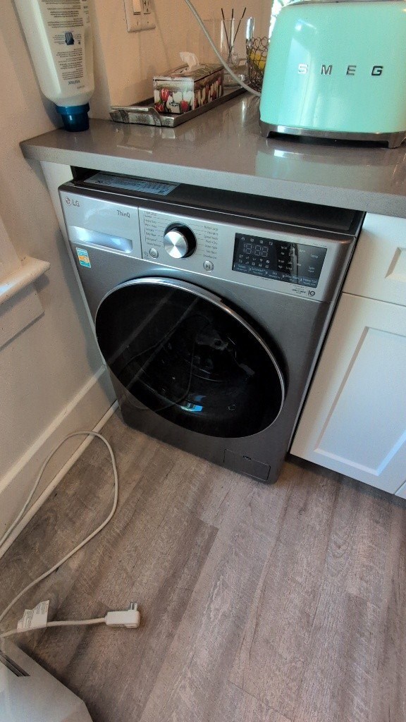 A washing machine with a black door is plugged into an outlet.