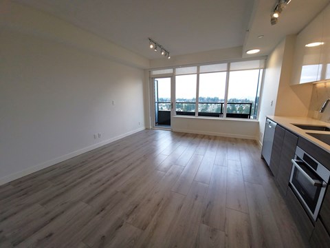 A spacious room with wooden flooring and a kitchen area to the right.