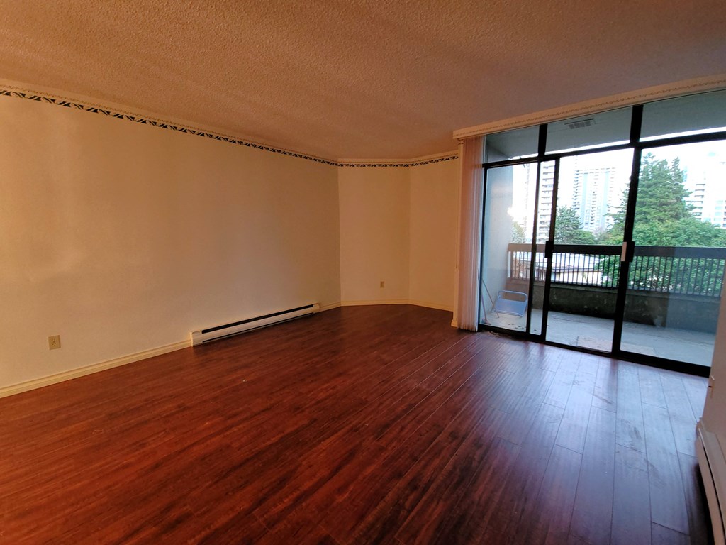 an empty living room with hardwood floors and a sliding glass door to a balcony
