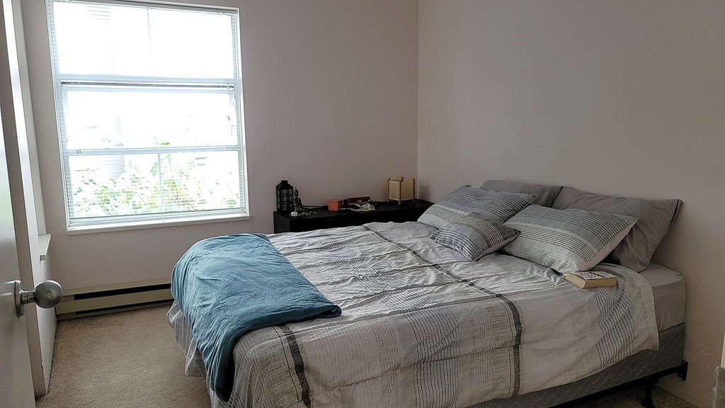A bed with a blue blanket and pillows in a room with a window.