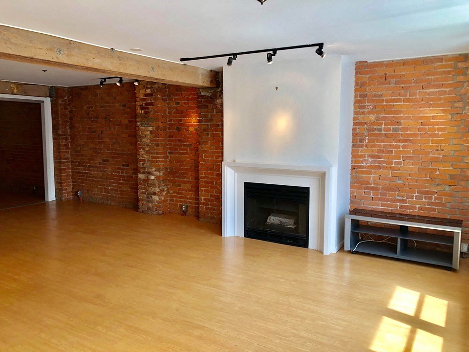 an empty living room with a brick fireplace and wooden floors