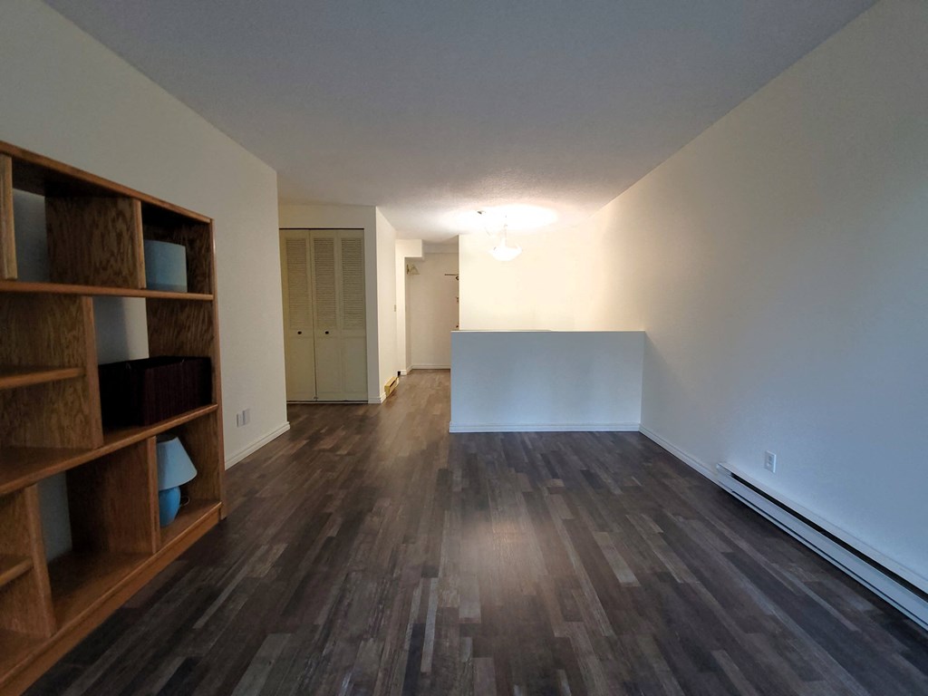 an empty living room with wood flooring and a white wall