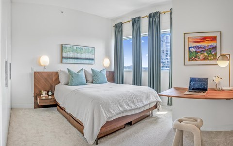 A bedroom with a large bed, a desk with a laptop, and a painting on the wall.