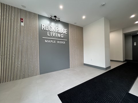 A hallway with a black carpet and a wall with a sign that says Rockridge Living Maple Ridge.