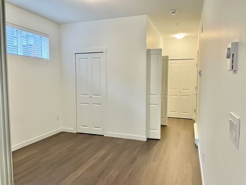 A room with white walls and wooden flooring with a door on the left.