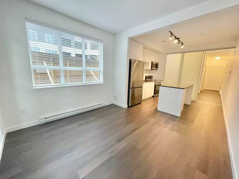 A spacious room with a kitchenette and a window with blinds.