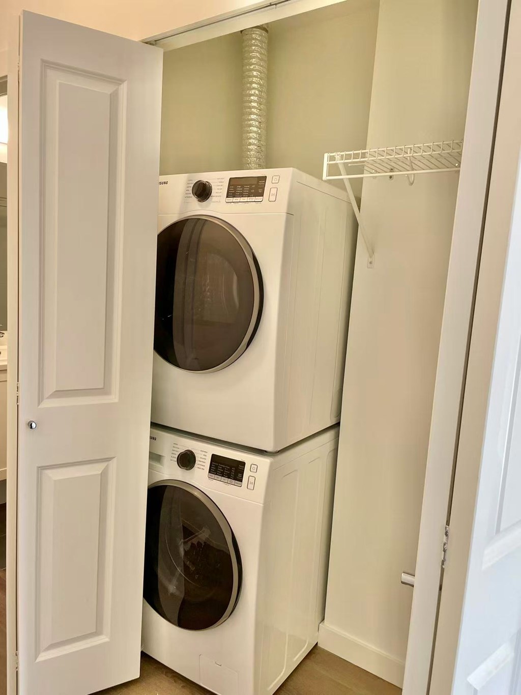 A white door is open to a laundry room with a washer and dryer stacked on top of each other.