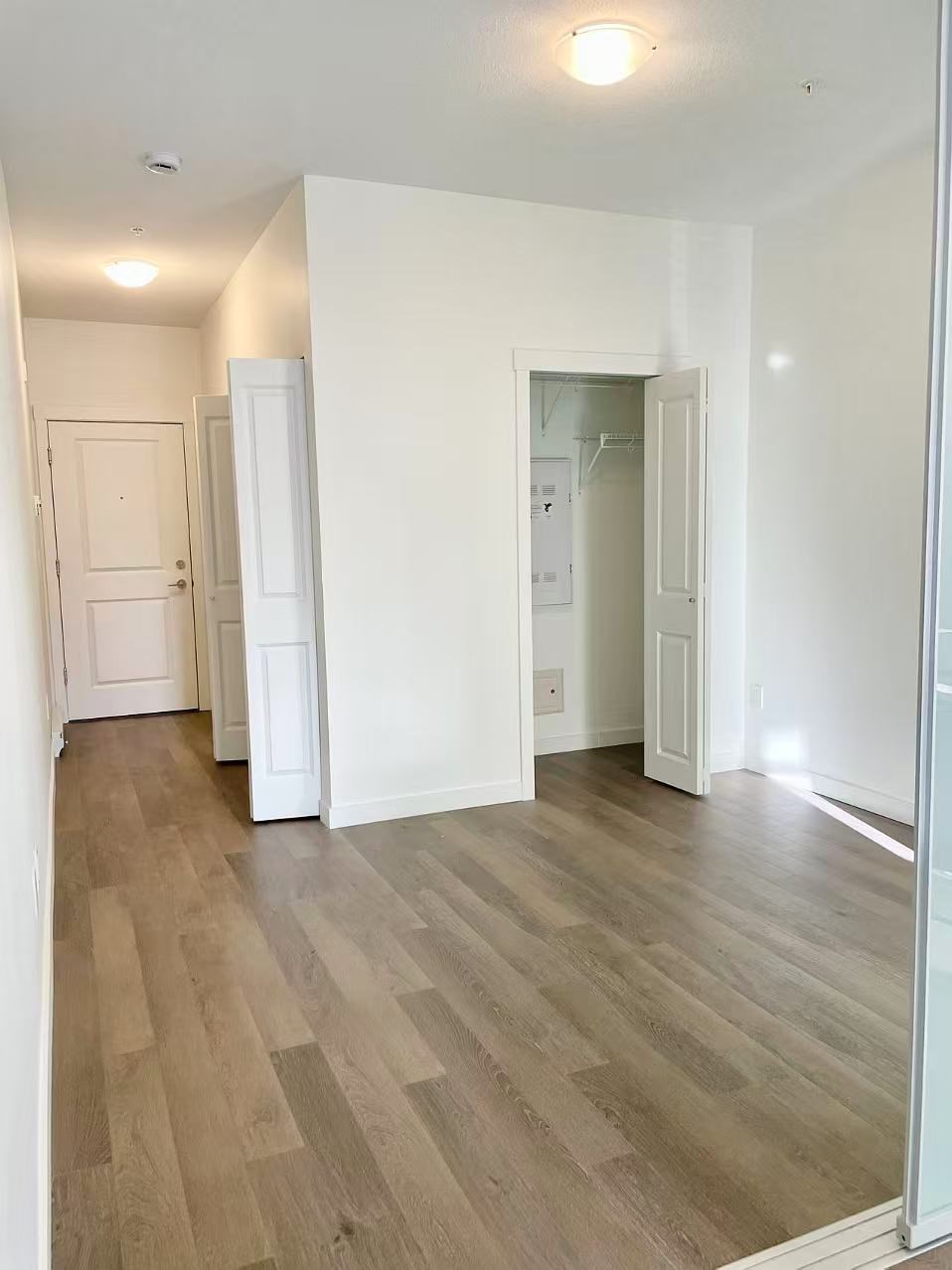 A room with white walls and wooden flooring with a door on the left and an open doorway on the right.