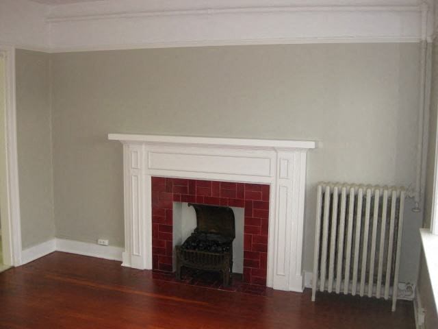 A fireplace with a white mantle and a red brick surround sits in a room with a wooden floor.