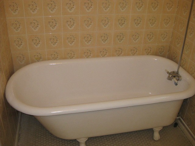 A white bathtub with a silver faucet is in a bathroom with a tiled wall.