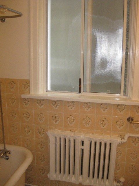 A white radiator is installed under a window in a bathroom.