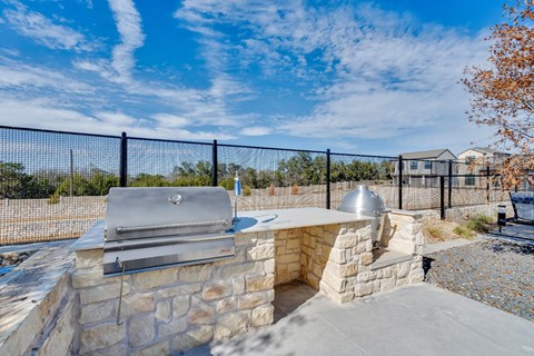 A stone BBQ grill is on a patio with a black fence.