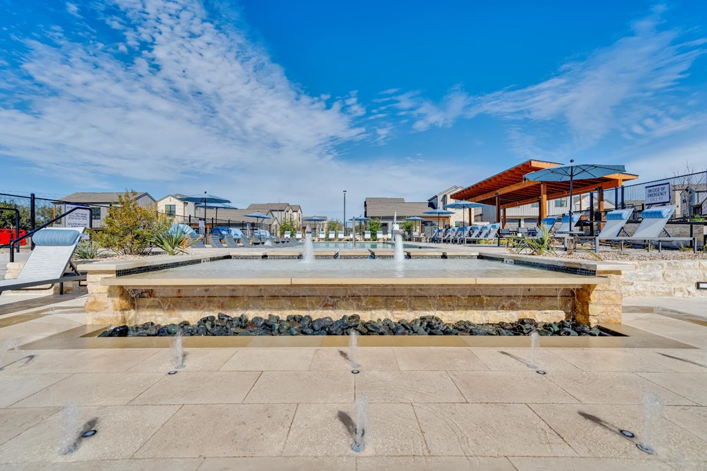 A fountain in the middle of a plaza with buildings in the background.