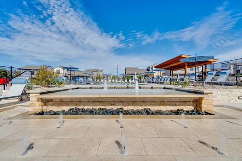 A fountain in the middle of a plaza with buildings in the background.