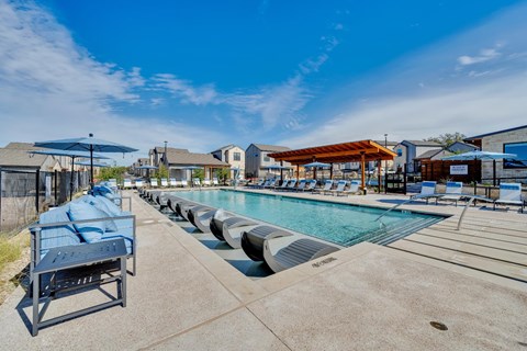 A sunny day at the pool with blue lounge chairs and a clear sky.