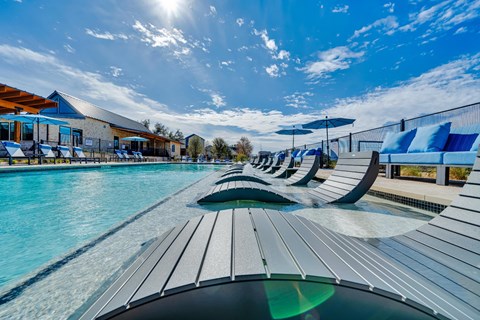A sunny day at the outdoor pool with blue water and sun loungers.