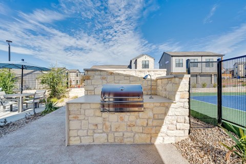 A backyard with a stone wall and a grill.