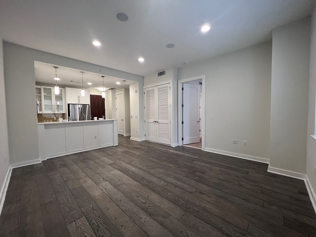 an empty living room with a kitchen and a door to a hallway