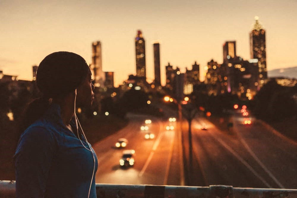 a woman standing on a bridge overlooking a city at sunset