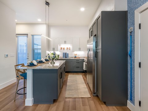 A modern kitchen with a dark grey refrigerator and wooden flooring.