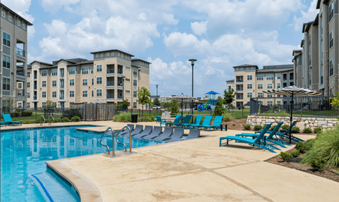 A swimming pool surrounded by blue lounge chairs and buildings in the background.