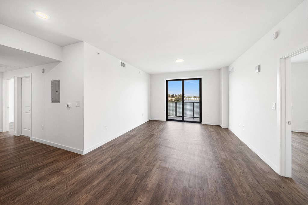 A living room with white walls and wooden floors and a door to a balcony