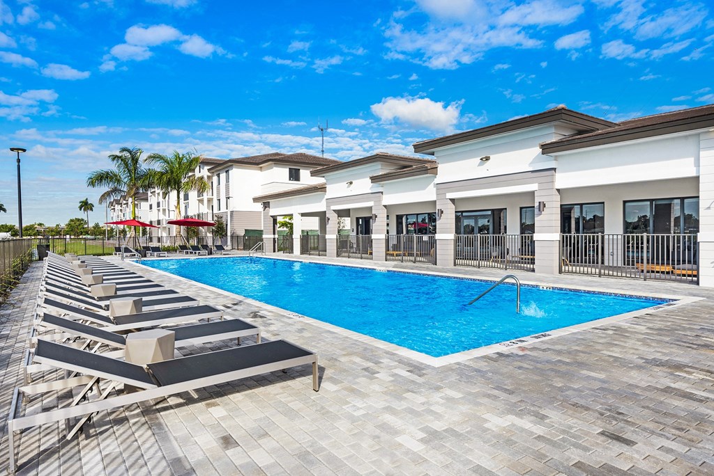 a swimming pool with lounge chairs and umbrellas in front of a building