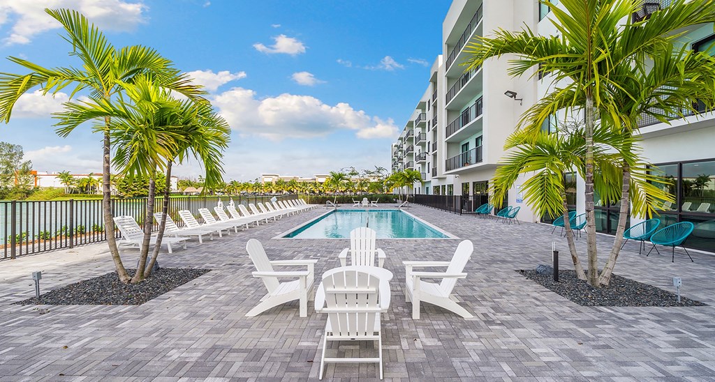 A pool with chairs and palm trees next to a building