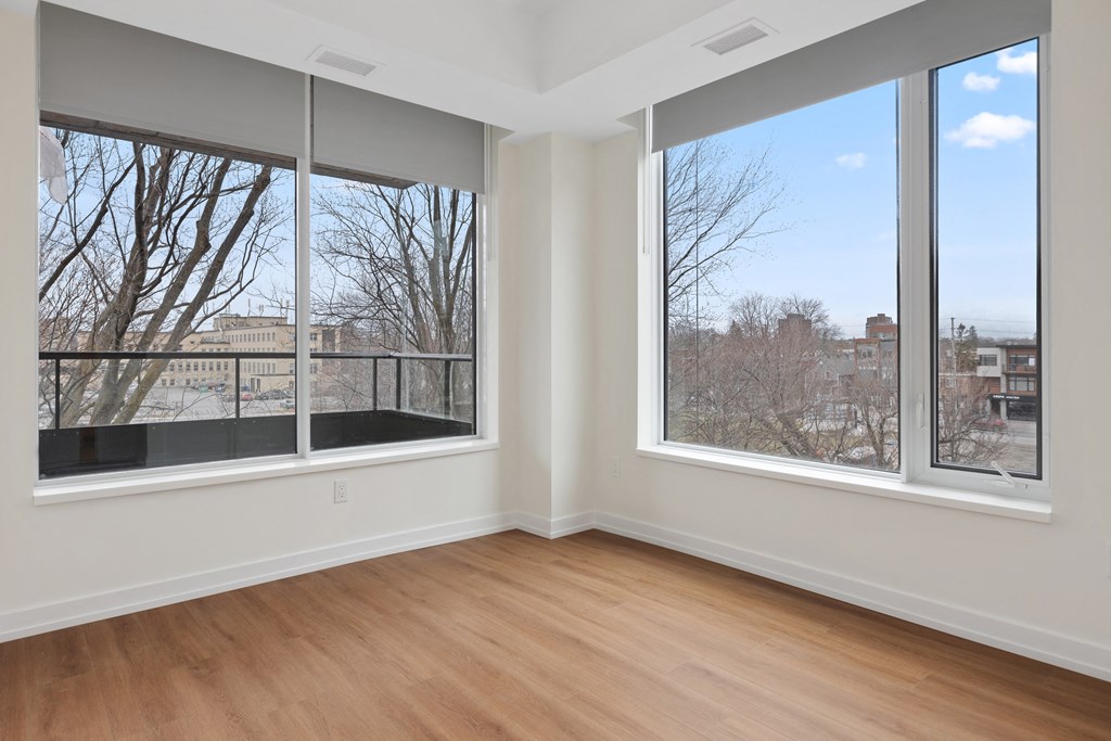 an empty living room with three large windows and a wooden floor