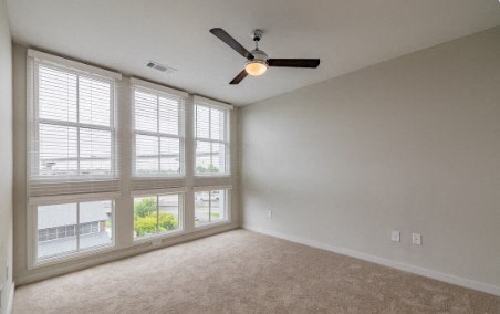 A room with a ceiling fan and large windows.