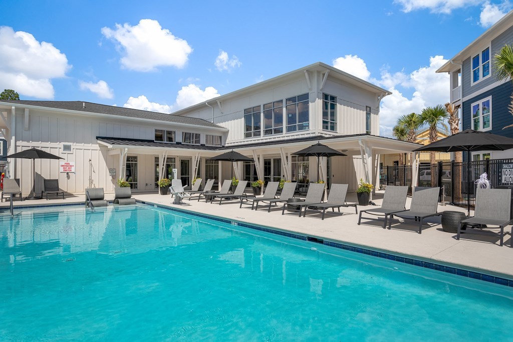 a swimming pool with chairs and umbrellas in front of a house
