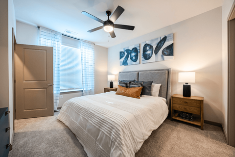 A bedroom with a large bed, a ceiling fan, and a painting on the wall.