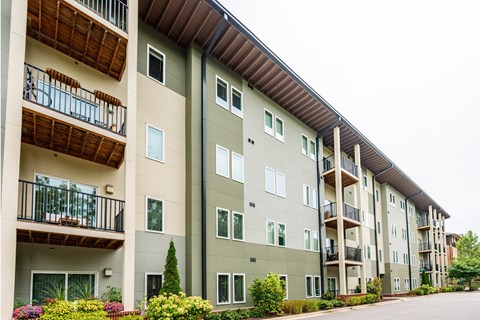 Apartment building with balconies and flower beds in front.